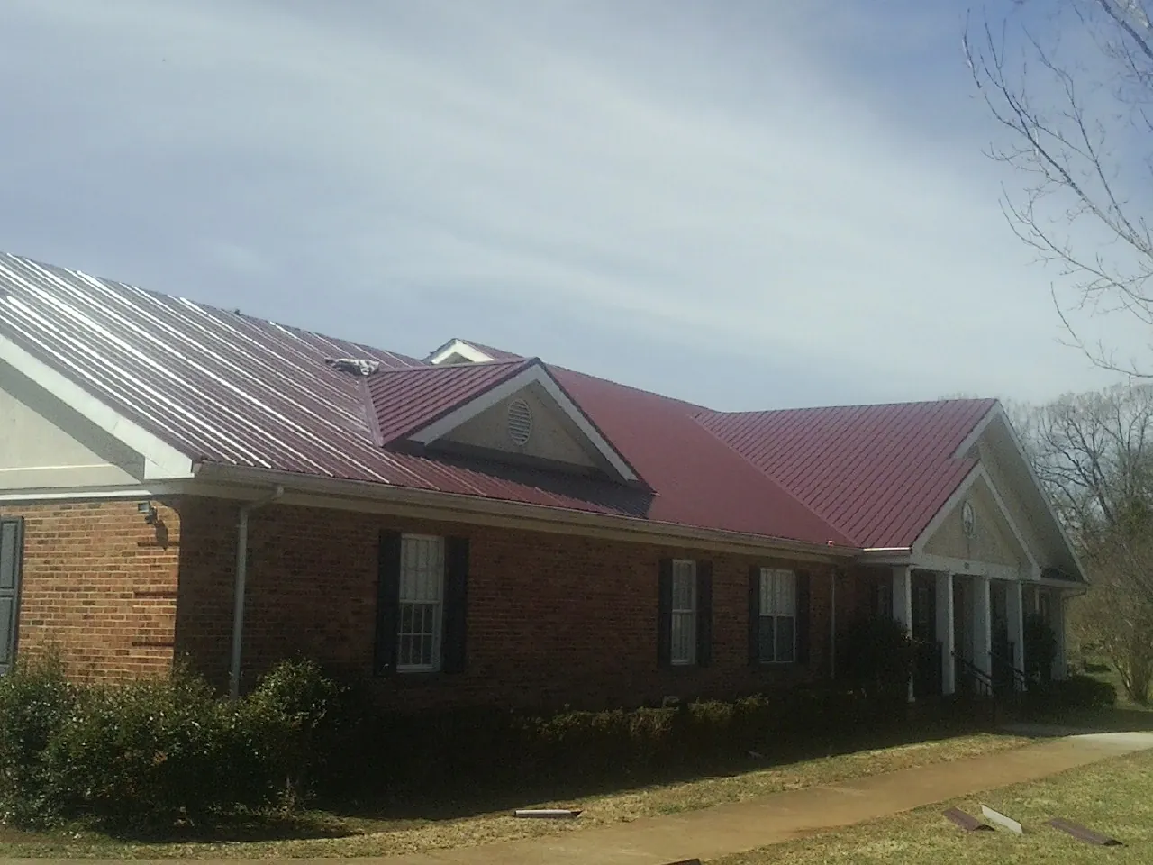 Red metal roof with gabled entries on a long brick building, from a Hail Damage Roof Repair job in Oronoco