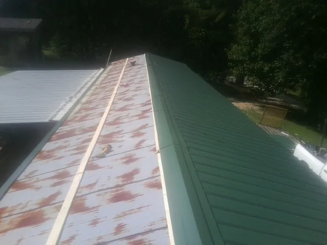 Old rusted panels beside newly installed green metal roofing — Wind Damage Roof Repair by Roofing Brothers in Oronoco