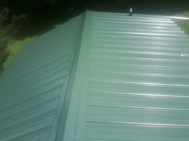 New green metal panels meeting at the ridge of a roof — Flat Roof Repair work by our crew in Oronoco