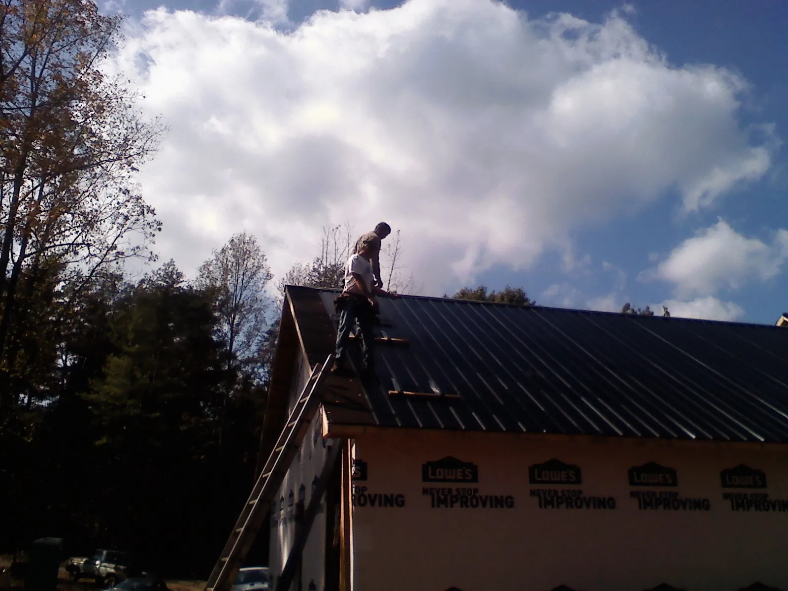 Roofer fastening dark metal panels high against a cloudy sky, from a Roof Inspection job in Oronoco