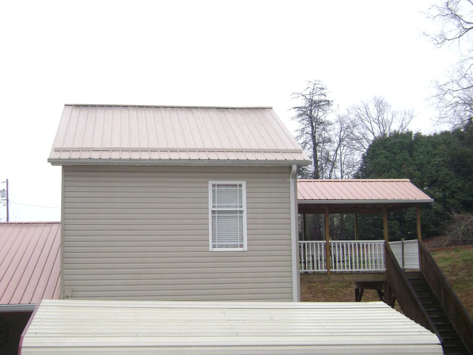 Tan metal roofs on a two story addition and attached porch, from a Roof Replacement job in Oronoco